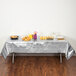 A table with food on it covered by a silver Creative Converting plastic table cover.