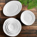 A group of Elite Global Solutions white irregular round melamine plates on a wooden surface.