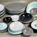 An irregular round mint green melamine plate on a wood surface with a stack of plates and bowls.