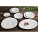 A group of white Elite Global Solutions Della Terra melamine plates on a wooden table.