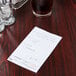 A white paper guest check on a table with a glass of brown liquid.