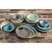 A gray Elite Global Solutions Cottage vintage bowl on a table with a stack of bowls and plates.