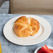 An Elite Global Solutions Cottage Vintage California melamine plate with a croissant on it next to a strawberry.