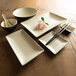A white Elite Global Solutions two-tone sauce dish on a wood surface with a spoon inside.
