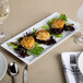A white rectangular melamine serving platter with three crab cakes on a white plate.