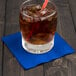 A glass with ice and a straw on a Cobalt blue beverage napkin.