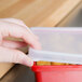 A person holding a clear plastic lid over a container with food.