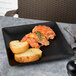 An Elite Global Solutions black square melamine plate with food on it on a table.
