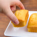 A hand holding a piece of food on a white rectangular melamine platter.