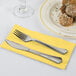 A fork and knife on a yellow Creative Converting dinner napkin.