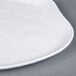 A close up of an Elite Global Solutions white melamine plate with an irregular edge on a gray surface.