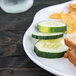 A white Elite Global Solutions melamine plate with a sandwich, cucumber slices, and potato chips on it.