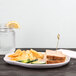 A white Elite Global Solutions melamine plate with a sandwich, chips, and a slice of orange on it.