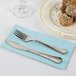 A fork and knife on a Creative Converting pastel blue paper dinner napkin on a plate with food.