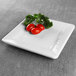 A white Elite Global Solutions square melamine plate with tomatoes and parsley on it.