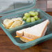 A jade GET 3-compartment take out container with a sandwich and chips in one compartment and grapes in another.