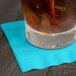 A glass of liquid with ice and a straw on a Bermuda Blue beverage napkin.