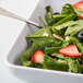 A white rounded square melamine bowl filled with a salad with strawberries and blueberries.