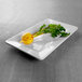 A white Elite Global Solutions rectangular melamine tray with a yellow vegetable on it.