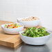 Three bowls of food including fruit and salad in white Coralline triangle melamine bowls.