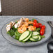 A plate with salad, shrimp, cucumber, and tomatoes on a table.