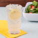 A clear plastic tumbler of water with ice and a lemon slice in it.