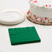 A white cake with red sprinkles next to an emerald green Creative Converting beverage napkin.