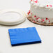 A white cake with red sprinkles next to a stack of cobalt blue Creative Converting beverage napkins.