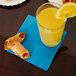 A glass of orange juice and a pastry on a turquoise blue beverage napkin.