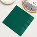 A stack of hunter green paper dinner napkins with a slice of white cake on top.