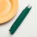 A fork and knife wrapped in a hunter green Creative Converting paper dinner napkin.
