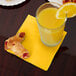 A glass of orange juice and pastries on a table with a Creative Converting School Bus Yellow beverage napkin.