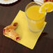 A glass of orange juice and pastries on a table with a yellow Creative Converting beverage napkin.