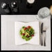 A white plate with a Snap Drape Reno ivory placemat on it, holding a salad with raspberries and nuts.