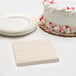 A stack of ivory beverage napkins with a white cake with red sprinkles next to a white plate.