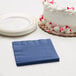 A white cake with red sprinkles next to a navy blue Creative Converting beverage napkin.