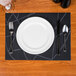 A dark navy Snap Drape Chico PVC placemat with a fork and spoon on it.