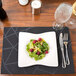 A dark navy Snap Drape Chico PVC placemat on a table set with a plate of salad and wine glasses.