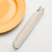 A fork and knife in a Creative Converting ivory paper napkin next to a plate.