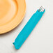 A fork in a Bermuda Blue paper dinner napkin next to a plate.