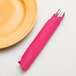 A fork in a Creative Converting hot magenta pink paper dinner napkin next to a plate.