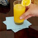 A hand holding a glass of orange juice with a pastel blue Creative Converting beverage napkin on a table.