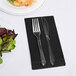 A fork and knife on a black velvet guest towel next to a plate of salad.