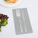 A Creative Converting Shimmering Silver guest towel with a fork and knife on it next to a plate of salad.
