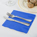 A fork and knife on a blue napkin next to a plate of food.