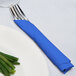A fork and knife wrapped in a cobalt blue Creative Converting luncheon napkin next to a plate of green beans.