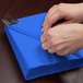 A person's hands wrapping a blue napkin around silverware with a knife.