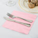A fork and knife on a Classic Pink Creative Converting napkin next to a plate of food.
