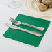 A Creative Converting emerald green luncheon napkin with a fork and knife on it next to a plate of food.