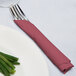A fork and knife wrapped in a burgundy napkin on a table.